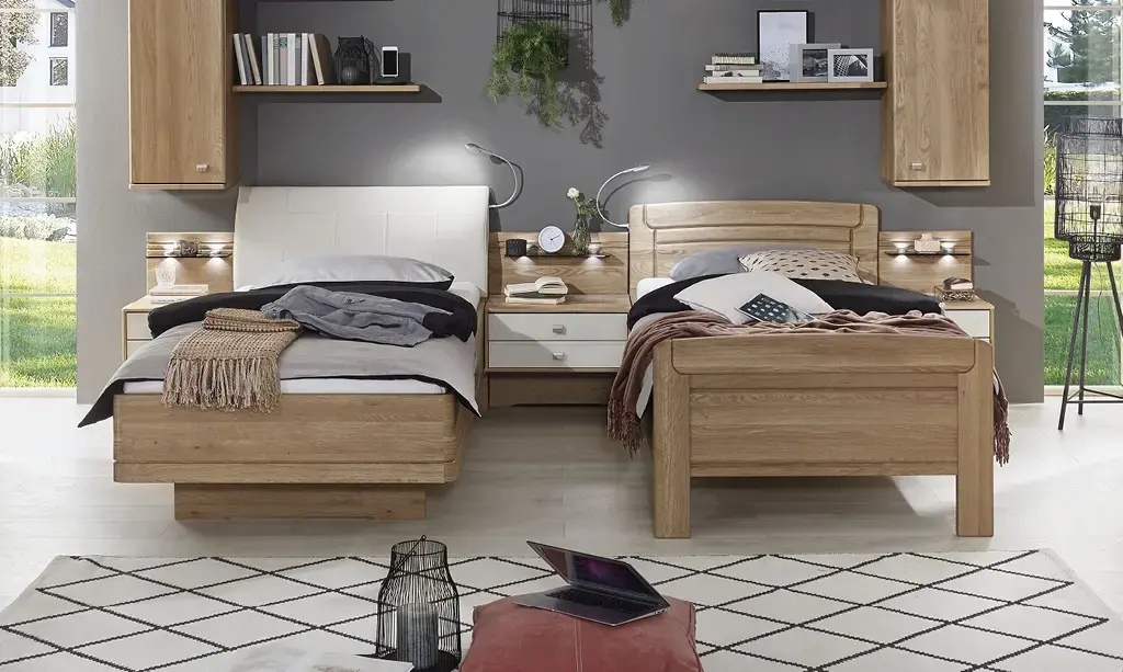 Zwei Einzelbetten aus Holz und Weiß mit Nachttisch in der Mitte, Wandregalen oben und grauer Wand im Schlafzimmer